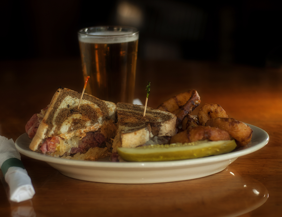 A Hotel Rueben sandwich with pickle and a lager beer in a glass.